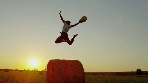 慢镜头MS无忧无虑的女人在田园诗般的乡村田野上跳干草在日落