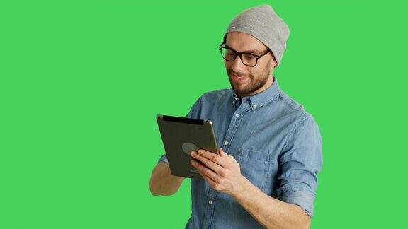 中景一个时尚的男人戴着帽子和眼镜使用平板电脑背景为绿幕