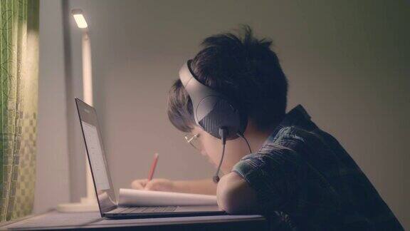 戴着眼镜的亚洲男孩坐在家里的一个房间里在线学习