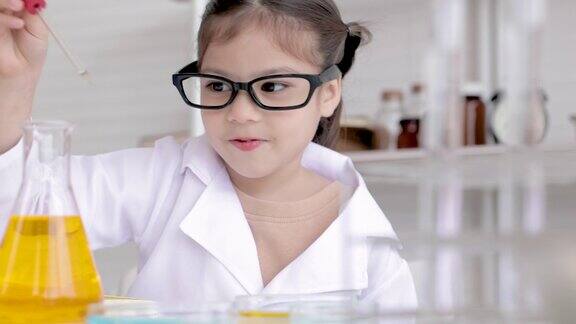 可爱的小女孩穿着实验服在学校实验室学习化学在科学课的桌子上做化学实验在玻璃中分析和混合液体
