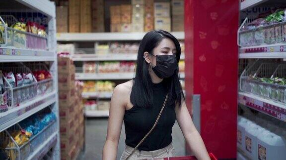 迷人的亚洲女人戴着防护面罩推着购物车在杂货店货物工厂仓库得到供应人类消费covid19新常态预算生活成本超市过道行走