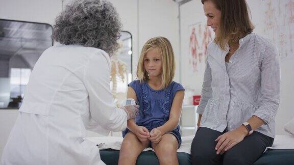 一个小学生坐在检查台上她的医生在检查她的血压