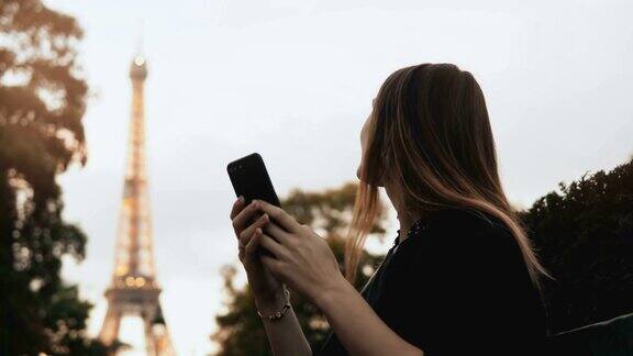 年轻漂亮的女人在用智能手机快乐的女性坐在长凳附近的埃菲尔铁塔在巴黎法国