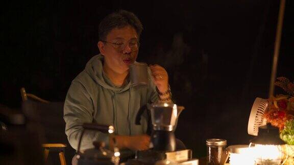 亚洲华人男旅行者晚上在露营帐篷里倒咖啡喝