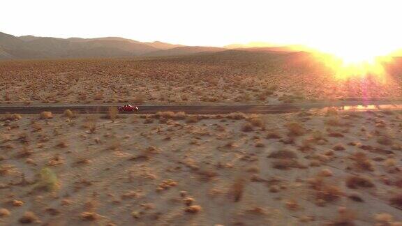 鸟瞰图红色经典车沿着荒凉的沙漠道路在日落