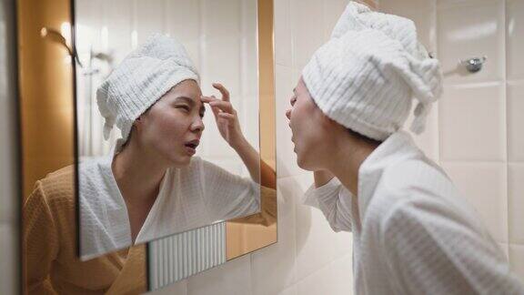 一个年轻的女人在浴室里对着镜子审视自己的脸