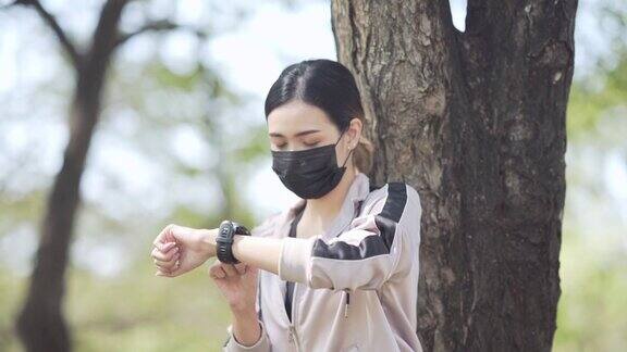 亚洲年轻女性锻炼防护口罩和看运动手表