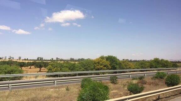 在炎热的沙漠中沿着绿树和植物的高速公路上移动的汽车窗口视图