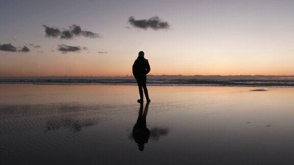 日落时分站在反射性沙滩上的女人