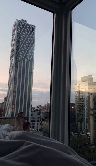 卧室里的女人透过全景窗户可以俯瞰曼哈顿的摩天大楼