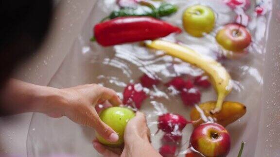女性洗手黄瓜辣椒西红柿香蕉梨苹果柠檬洗手新鲜蔬菜和水果用水在盆中慢动作素食新的收获洗水果和蔬菜
