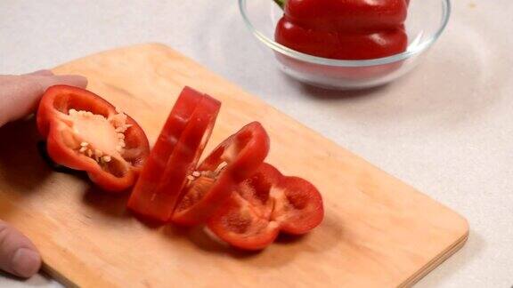 男子手的特写镜头在切菜板上切红辣椒然后把它放在一个玻璃碗里