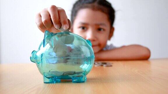亚洲小女孩在泰国幼儿园学生制服把硬币放入清晰的小猪存钱罐选择以猪存钱为教育理念