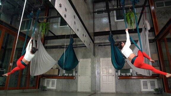 迷人的体贴的年轻女子做空中瑜伽姿势使用吊床