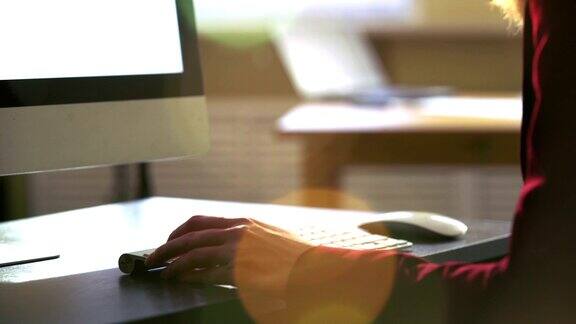 一个年轻女子在一张桌子前用电脑键盘工作太阳光的光学耀斑