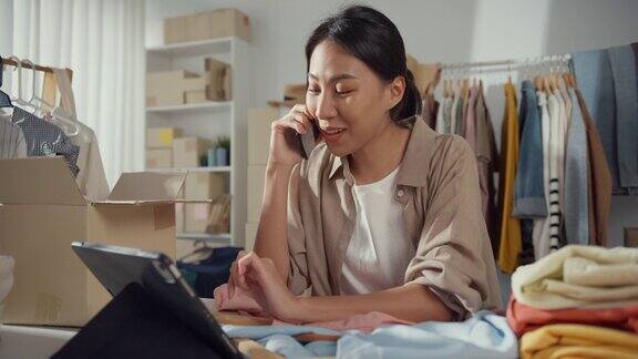 年轻的亚洲小企业主女性使用手机接收订单并在家里用平板电脑检查库存