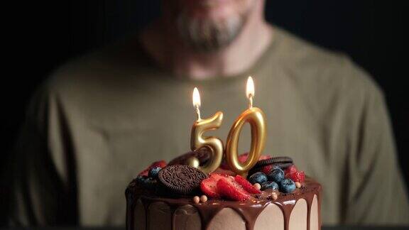 五十岁的男人在燃烧着五十根蜡烛的巧克力蛋糕前许愿50周年生日蛋糕慢动作