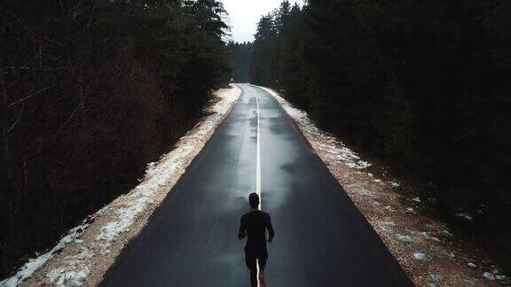 年轻的跑步者在往山上的路上跑步无人机从上面拍摄的一个跑步者年轻的运动员在寂静的秋天荒芜的关隘无人机电影后视图