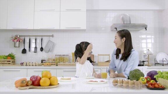 快乐的亚洲家庭妈妈和小女孩在家里的厨房里吃早餐麦片加牛奶和橙汁健康食品理念为了增强身体的力量慢动作
