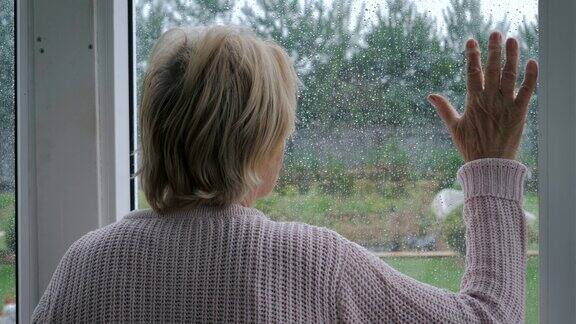 下雨时伤心的老妇人把手放在玻璃上望着窗外的希望