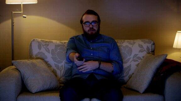 一个男人坐在客厅的沙发上看电视换频道落地灯打开