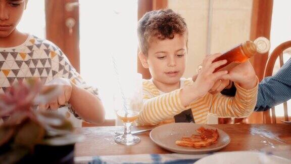 小男孩在和家人吃早餐时往煎饼里加蜂蜜