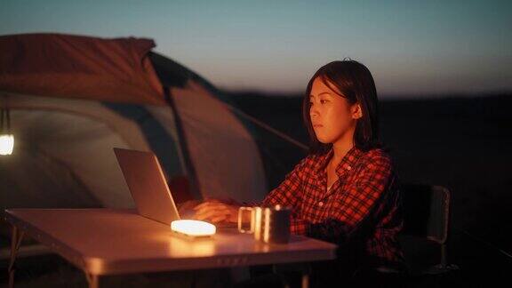 在野外露营时一名年轻女子在帐篷旁使用笔记本电脑