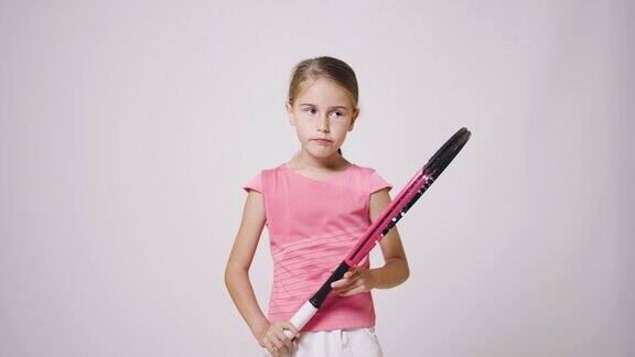 年轻的女网球运动员拿着球拍穿着粉色运动服的女孩感到无聊和愤怒