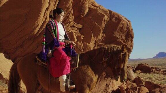 一个十几岁的美国印第安女孩穿着传统的纳瓦霍服装坐在她的马在纪念碑谷沙漠在亚利桑那州犹他州在一个大的岩石组在一个晴朗明亮的日子