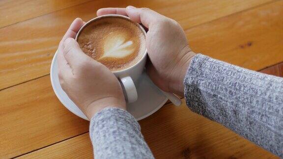 女人手握拿铁咖啡在木桌上摄影