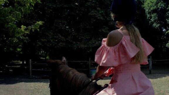 一个十几岁的女孩戴着保护头盔穿着粉红色的衣服骑着一匹棕色的马背景是树木侧视图4k4k的视频