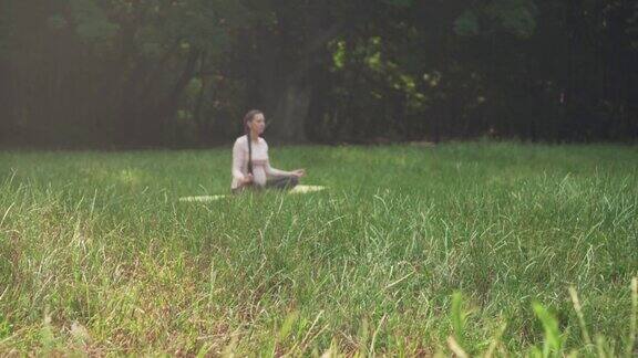 一位孕妇坐在公园的地毯上练习瑜伽以莲花的姿势坐着冥想