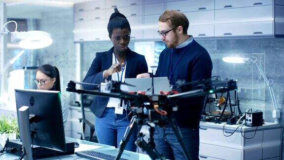 白人男性和黑人女性工程师在一个无人机项目的帮助下笔记本电脑和做笔记他在一个明亮的现代化高科技实验室工作
