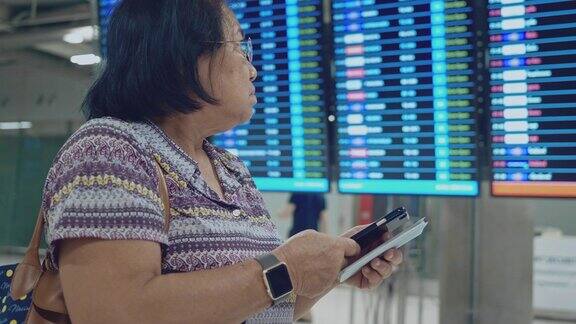 亚洲资深女性在到达离境板上检查和查看航班