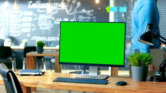 个人电脑与模拟绿色屏幕显示器站在办公桌上在后台的人在白天在创意办公室工作