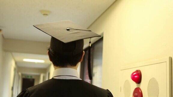 亚洲学生戴着学士帽穿着学位服走在走廊上