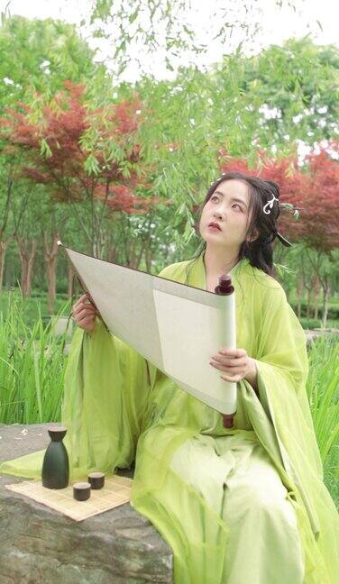 一位身着汉服的中国美女正在户外欣赏书画