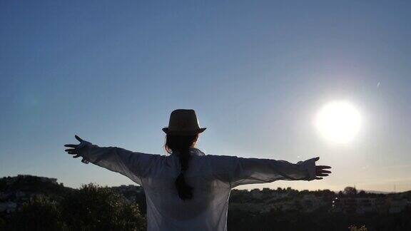 女孩站在山顶看着城市和大海在日落的时候举起她的手向太阳