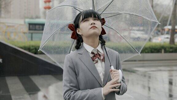 日本女学生穿着校服打着透明的雨伞站在雨中