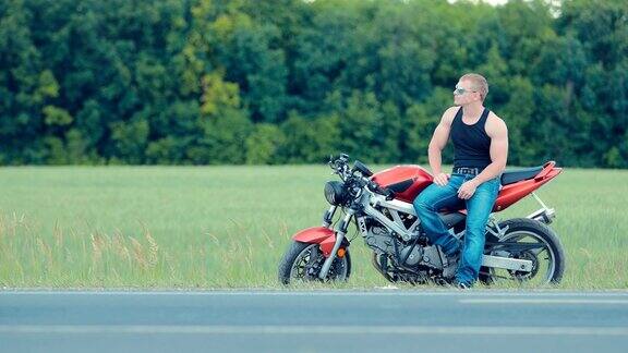 侧面的美丽的摩托车手坐在站在摩托车座位的一边模糊的背景
