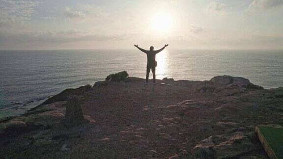 成功的人举手做成功的手势达到顶峰的幸福海边岩石上的剪影