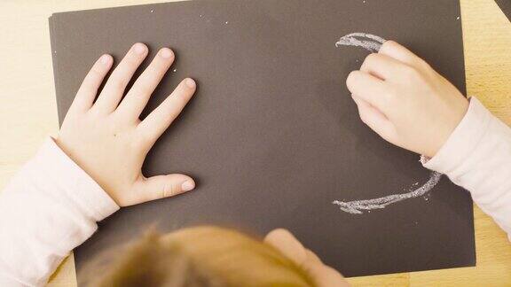 一个女孩在一张桌子上用蜡笔在纸上画画