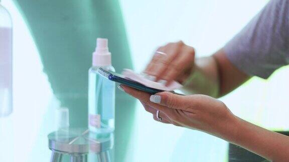 女性使用酒精喷雾剂擦拭智能手机表面清洁和保护COVID-19