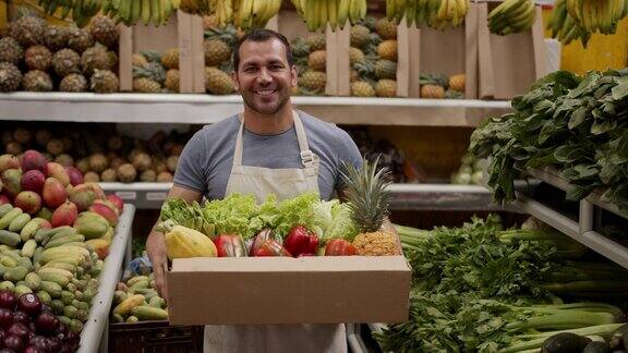 一名友善的男子正准备在一个装满新鲜水果和蔬菜的纸箱里为顾客送货微笑着看着相机