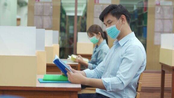 两名亚洲大学生戴口罩坐在图书馆社交距离6英尺的地方以避免新冠病毒在大学内传播