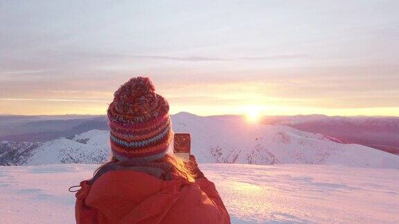 冬季一名女性高山攀登者在高海拔的山峰上用手机拍照