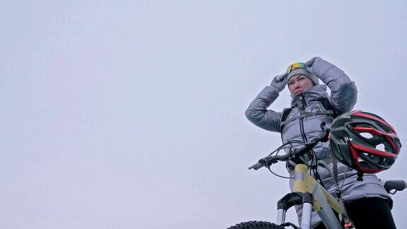 女人穿着运动器材这个女孩穿着银色的羽绒服背着自行车背包戴着头盔结冰的贝加尔湖的冰自行车的轮胎上覆盖着特殊的尖钉