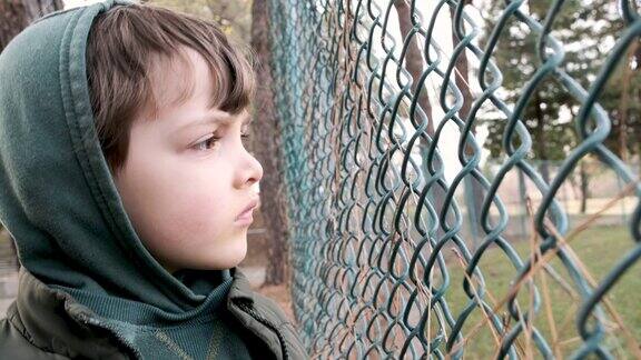 严肃沉思的孩子透过栅栏望着