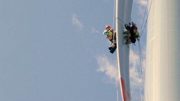 史诗近距离观察两名专业绳索进入技术人员-工业攀登者工作在风力涡轮机的叶片上的绳索做检查技术员在包里寻找设备风轮机塔在右边天空和云彩在后面