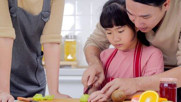 一个快乐的年轻家庭妈妈爸爸和小女孩在厨房里一起做饭泰国家庭